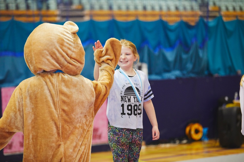 A child stands on a podium and high fives their club mascot