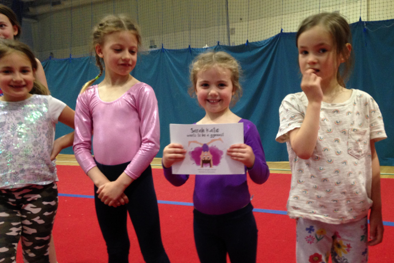 Emmy wins a prize - young girl holding a gymnastics book with girls  at class
