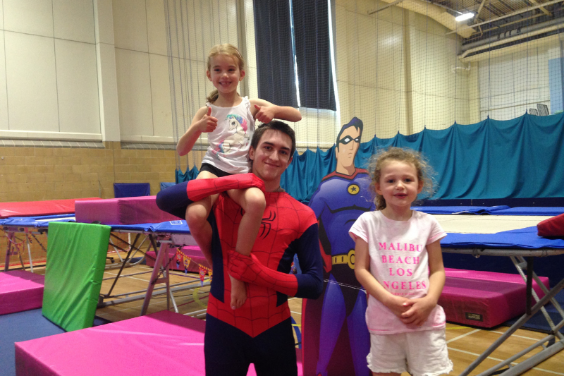 The gymnastics coach dressed as spiderman next to trampolines with two children