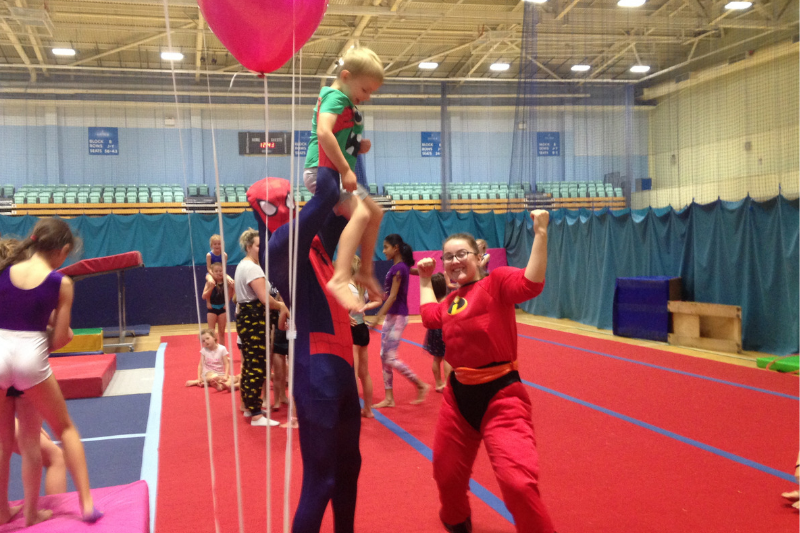A child is lifted up by two coaches dressed as superheroes