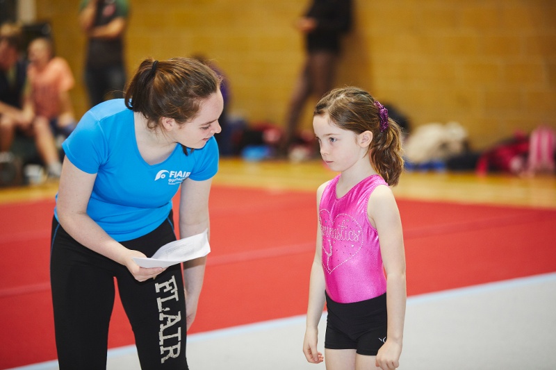 A gymnastics coach helps their student. 